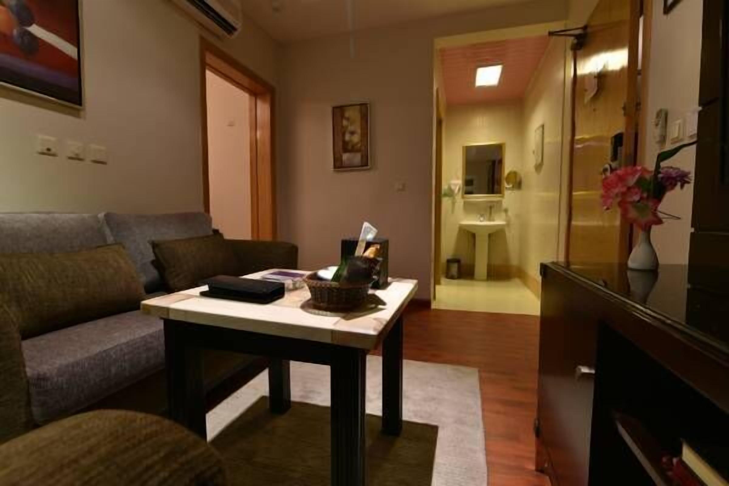 A living room with a sofa, a coffee table, and a television. There is a doorway leading to a bathroom.