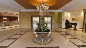 A lobby with a central round table, a chandelier, elevators, and a piano. - Boudl Al Maidan (Hafr Al Batin)
