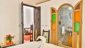 A hotel room with a bed, a mirror, a door leading to a bathroom, and a view of a red carpeted area.