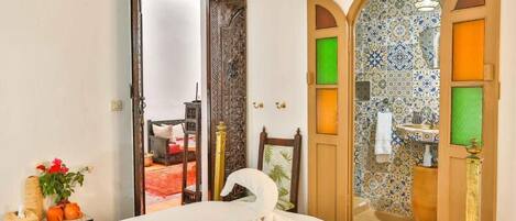 Habitación de hotel con cama, espejo, puerta que da a un baño y vista a un área alfombrada en rojo.