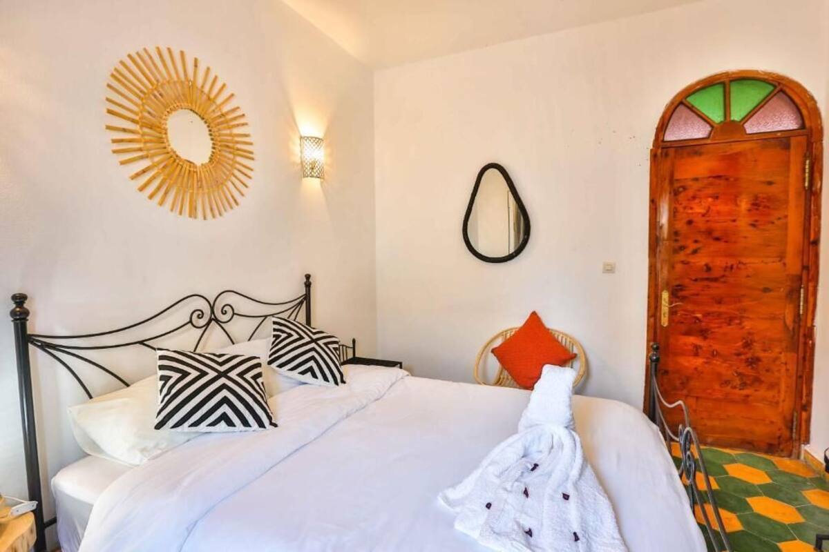 A neatly made bed with patterned pillows, a wall-mounted mirror, and a wooden door with a green and yellow patterned floor.