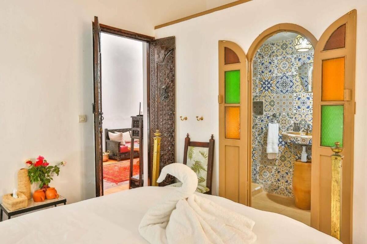 A hotel room with a bed, a mirror, a door leading to a bathroom, and a view of a red carpeted area.