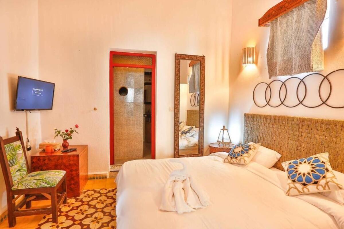 A hotel room with a bed, a television, a chair, a desk, a mirror, and a door.