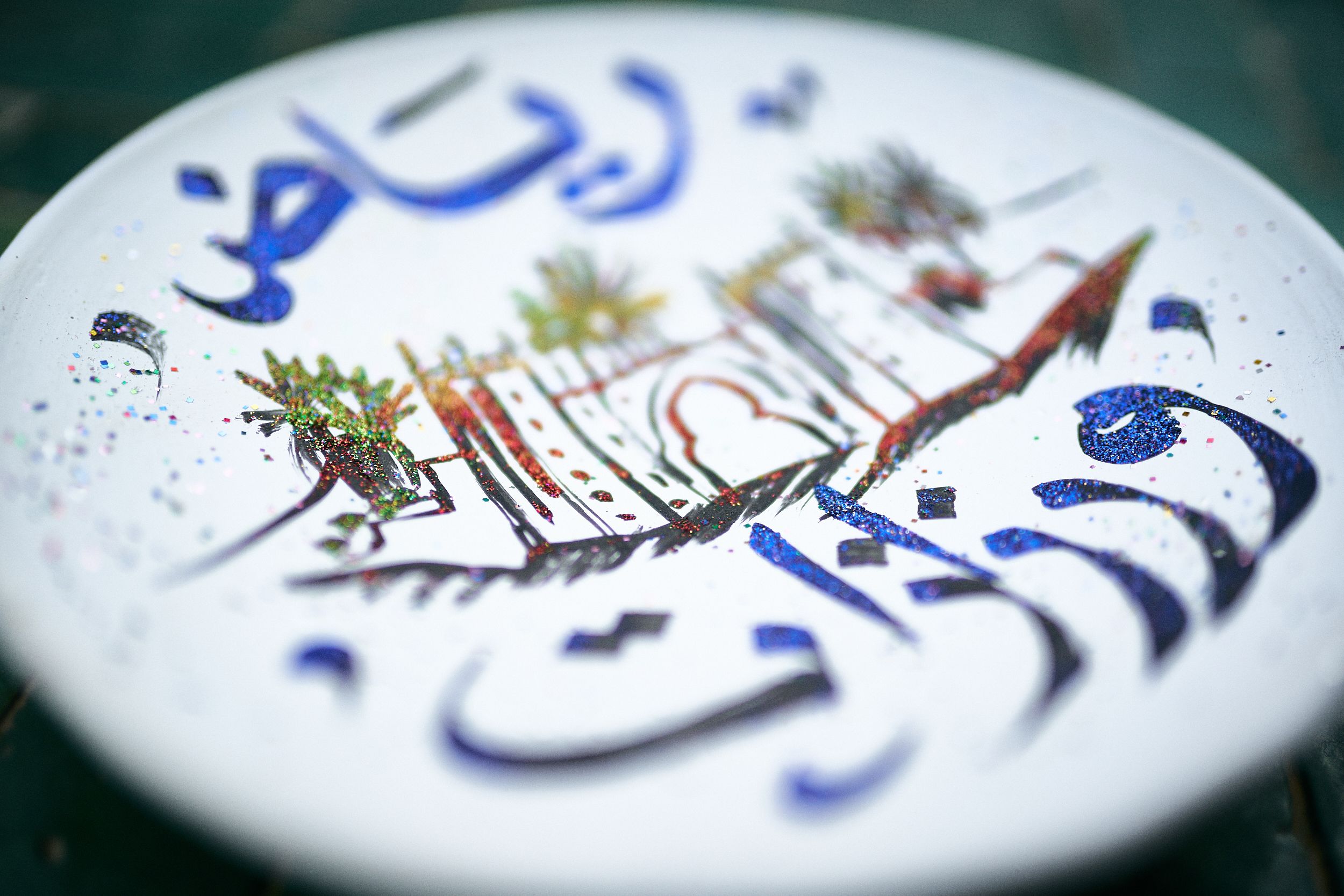 Primer plano de un plato decorativo con caligrafía árabe y un paisaje estilizado.