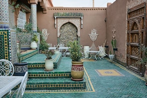 A courtyard with a tiled floor, steps, potted plants, and outdoor furniture. - Riad Ouarzazate (Ouarzazate)