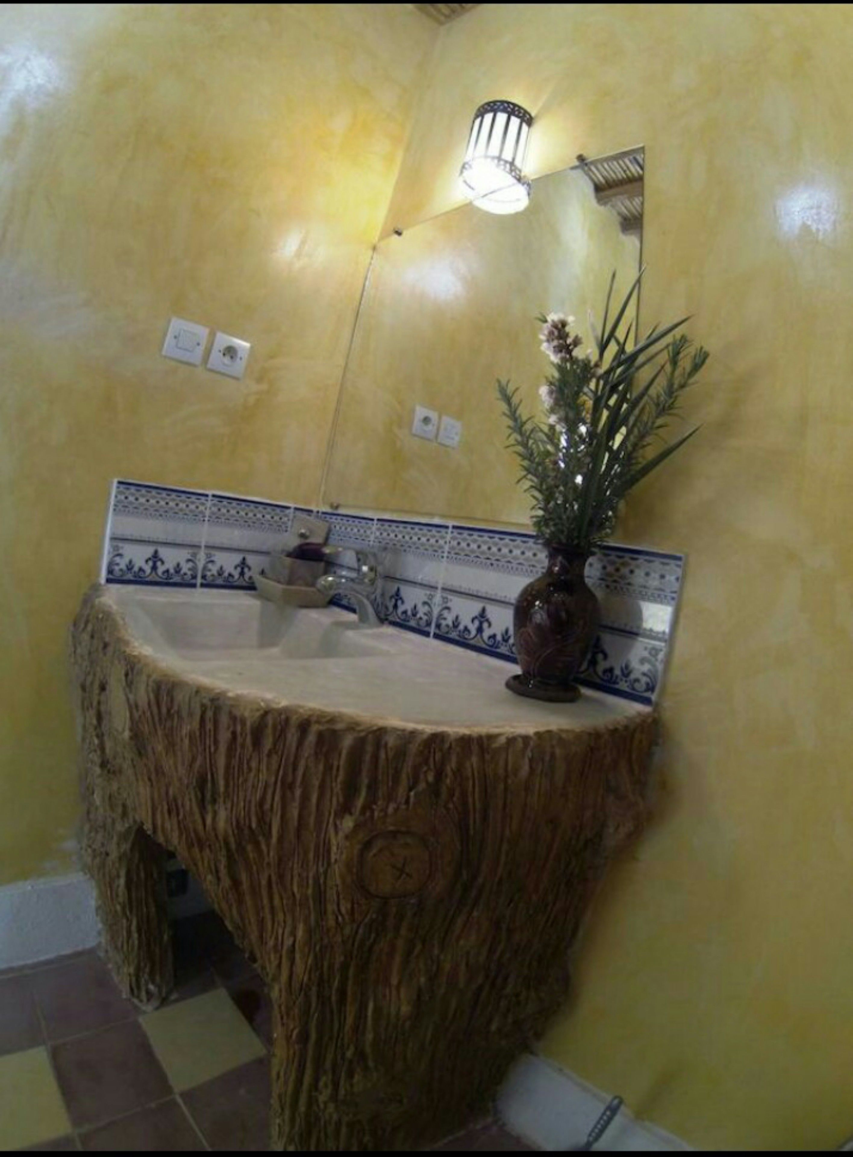 A bathroom with a unique tree stump sink, a mirror, and a decorative plant.