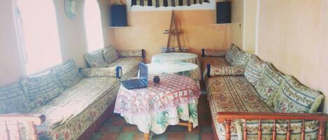 A traditional room with a sofa, a small table with a laptop, and a patterned wall hanging.