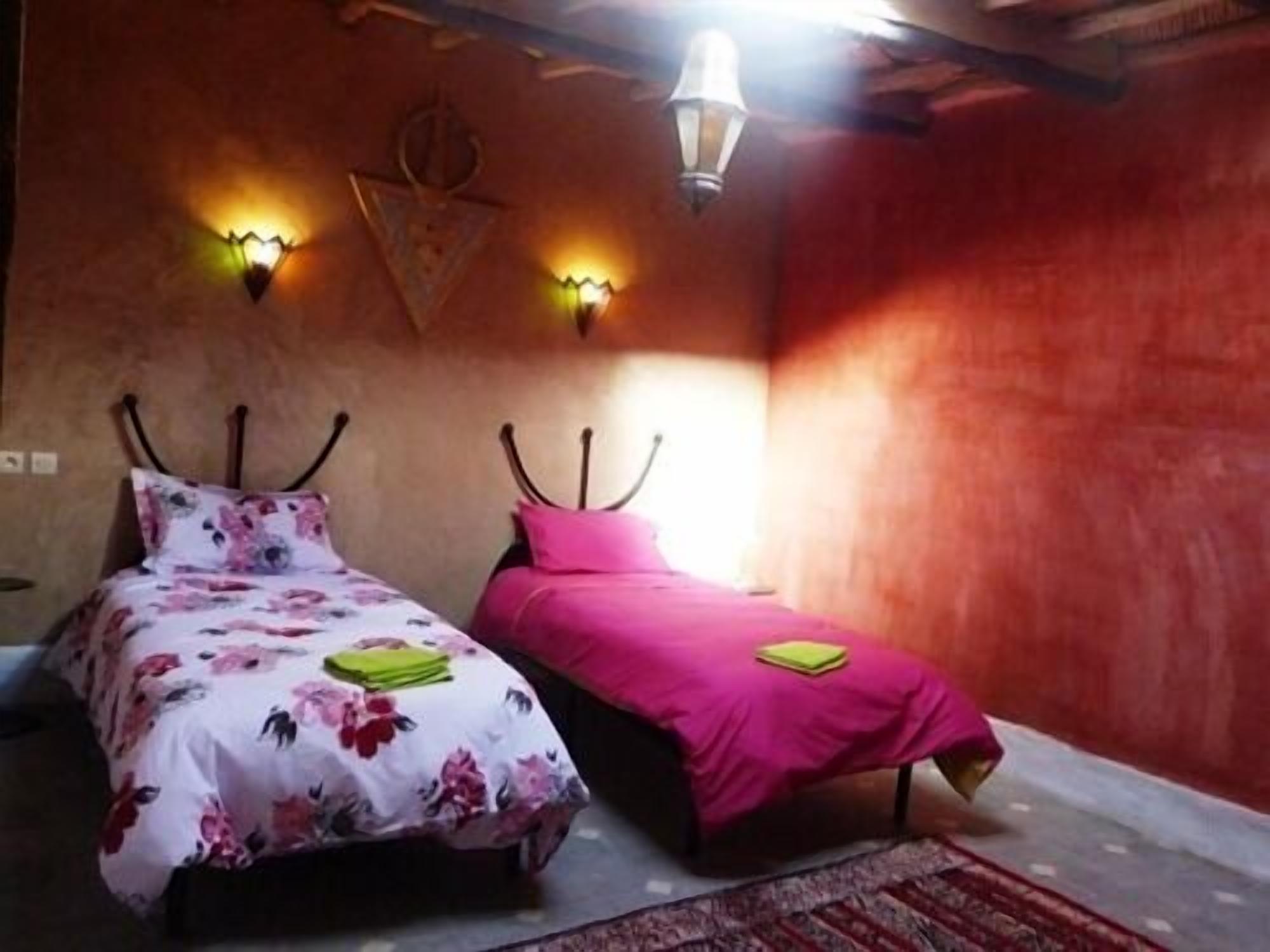 Un dormitorio con dos camas, cada una con un edredón de diferente color, y una lámpara de pared.