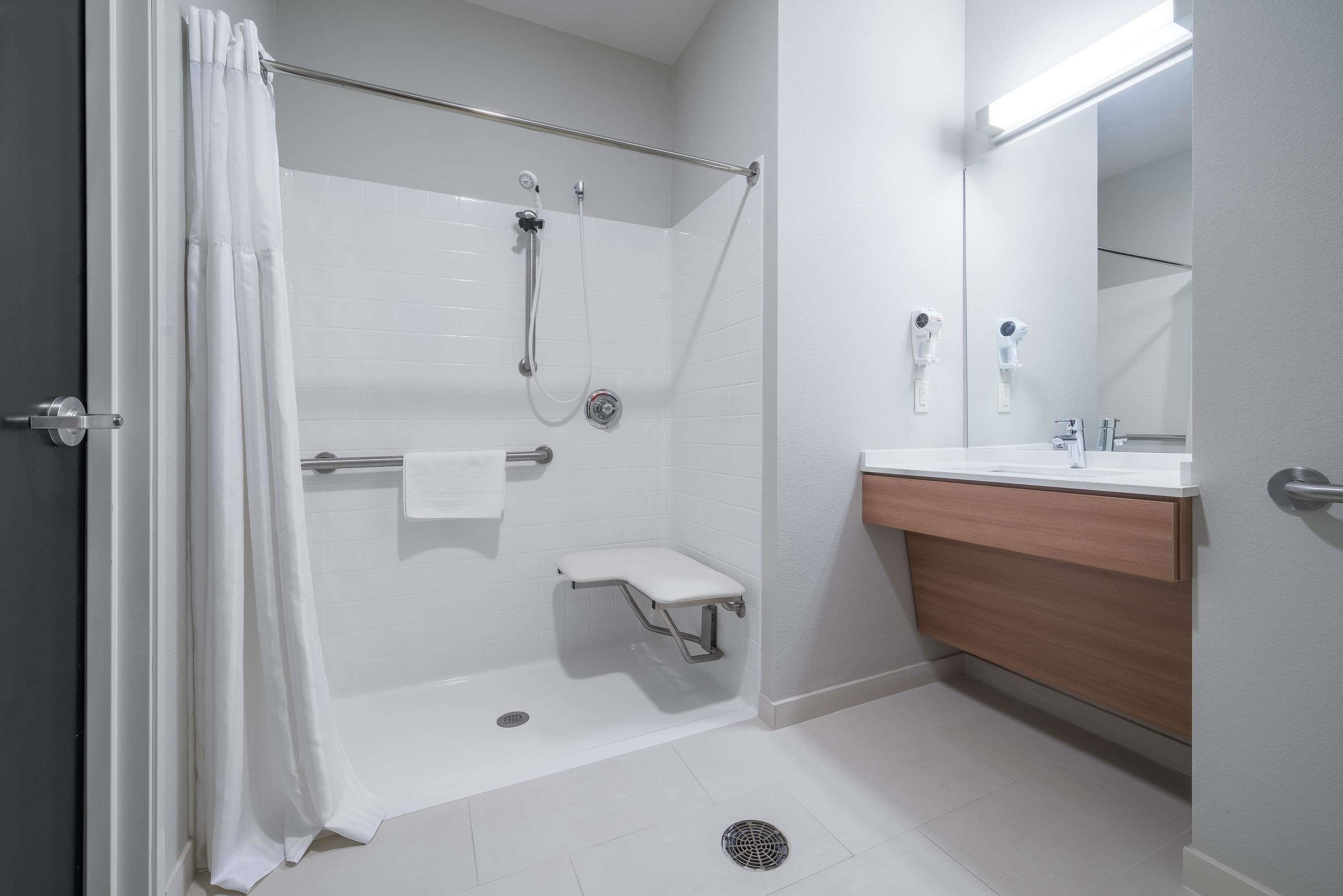 A modern bathroom with a walk-in shower, a small bench, a towel rack, and a vanity with a mirror.