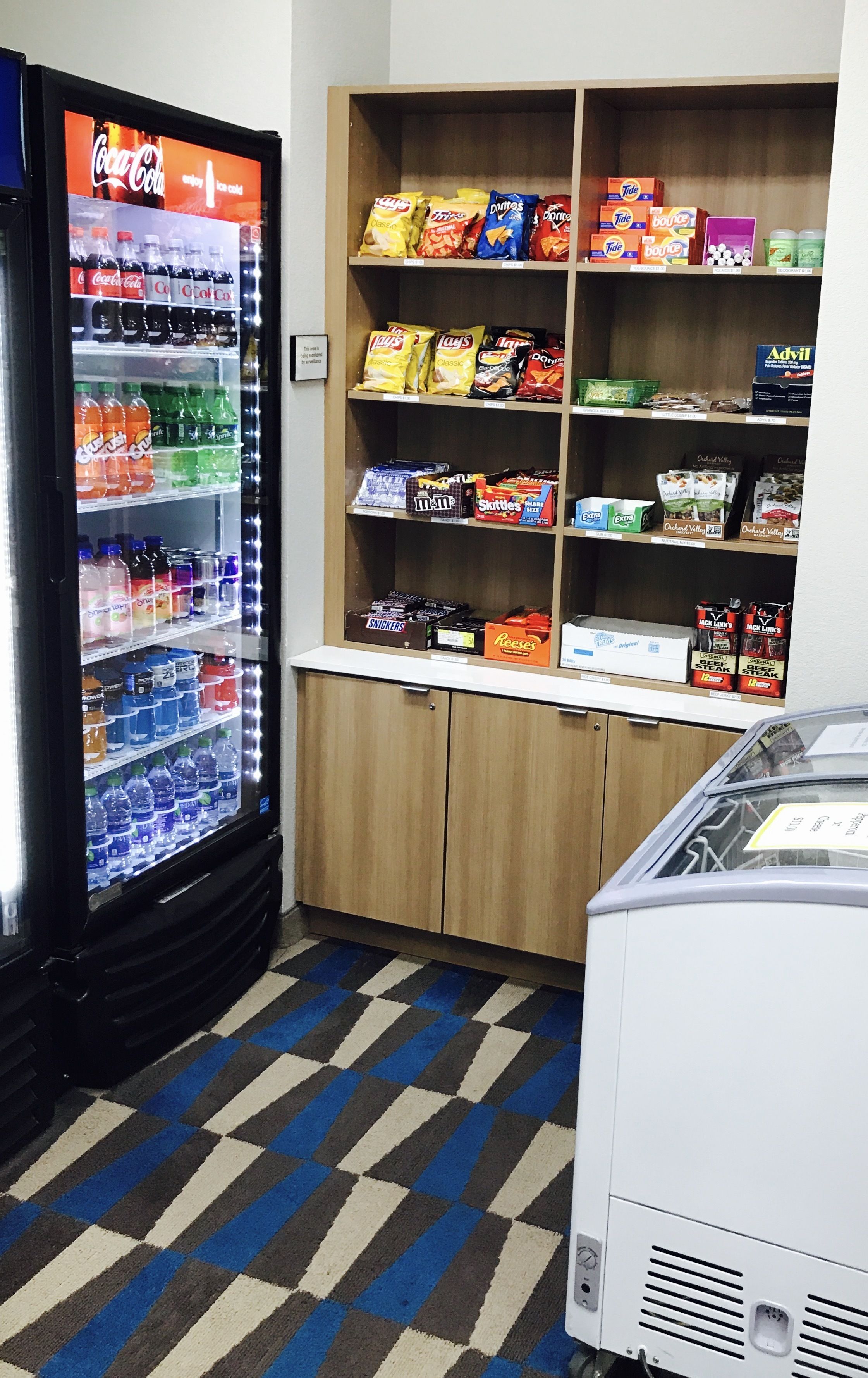 A vending machine stocked with snacks and beverages, a small counter with packaged goods, and a refrigerator.