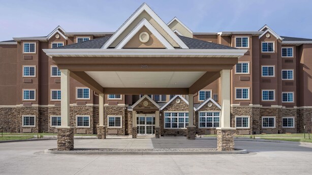 A multi-story hotel with a covered entrance, stone pillars, and a clear sky. - Microtel Inn & Suites By Wyndham Moorhead Fargo Area (Moorhead)