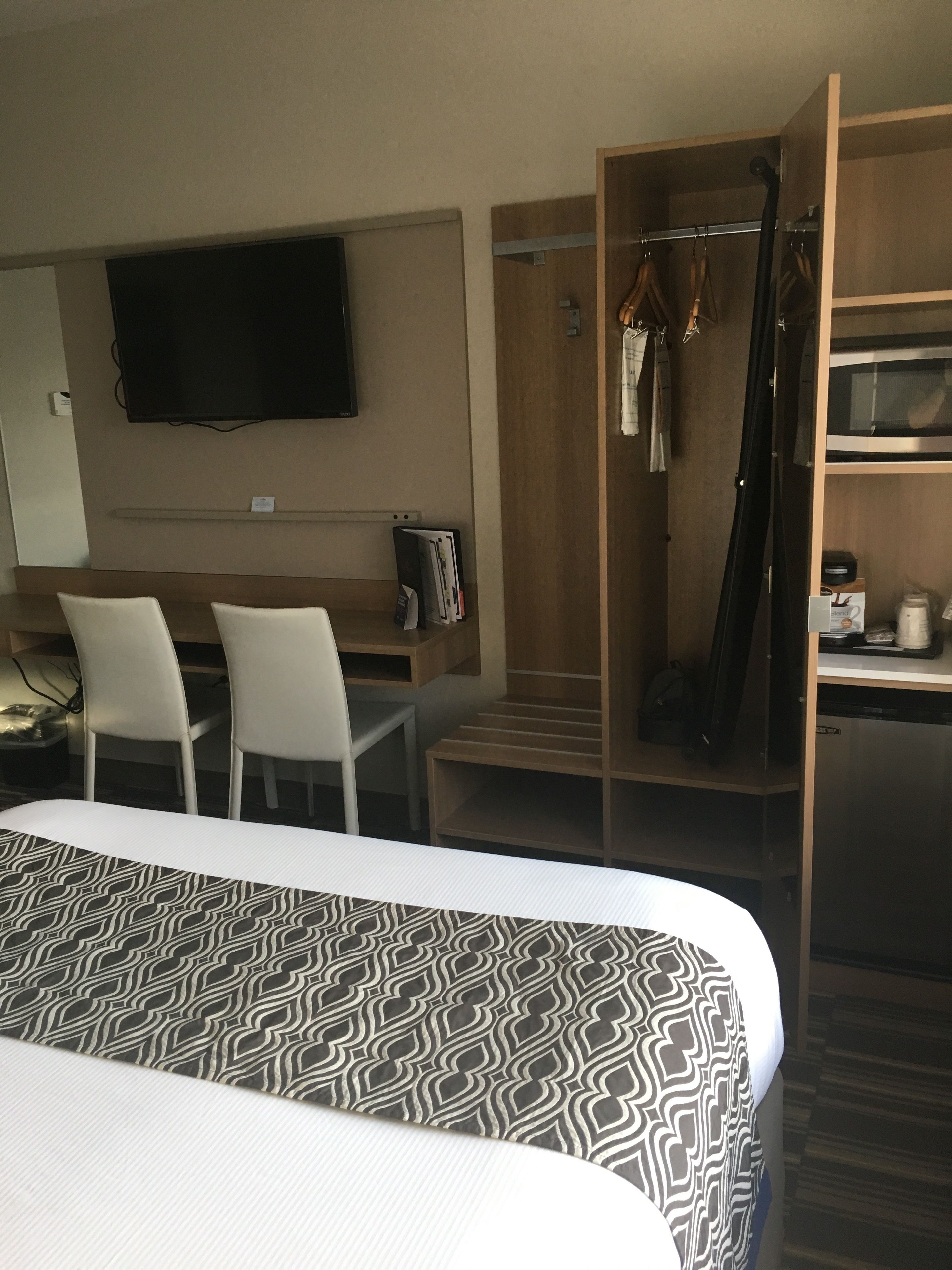Ein Hotelzimmer mit einem Bett, einem Schreibtisch mit zwei Stühlen, einem an der Wand befestigten Fernseher, einem Holzschrank und einer Mikrowelle.