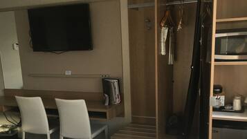 Ein Hotelzimmer mit einem Bett, einem Schreibtisch mit zwei Stühlen, einem an der Wand befestigten Fernseher, einem Holzschrank und einer Mikrowelle.