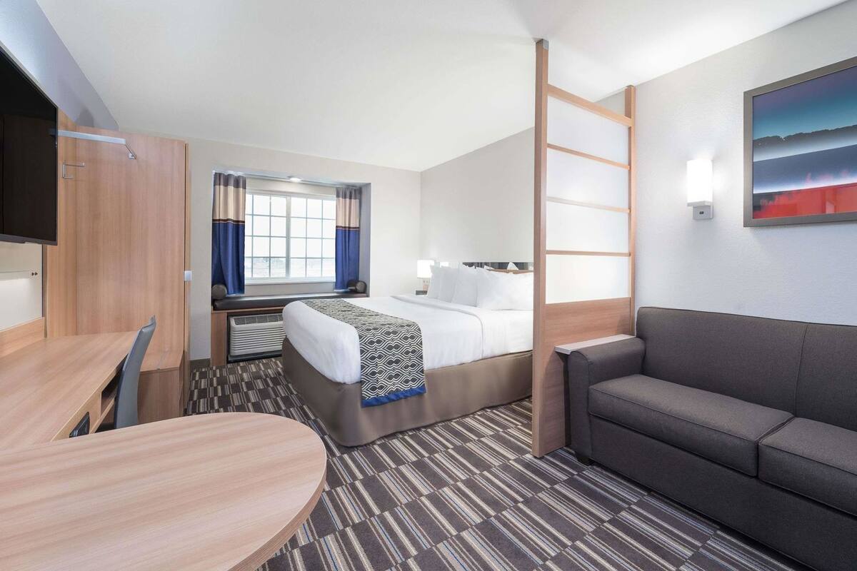 A hotel room with a bed, a sofa, a desk, a TV, and a window with curtains.
