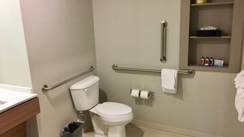 A bathroom with a toilet, grab bars, a trash can, and a shelf with toiletries.