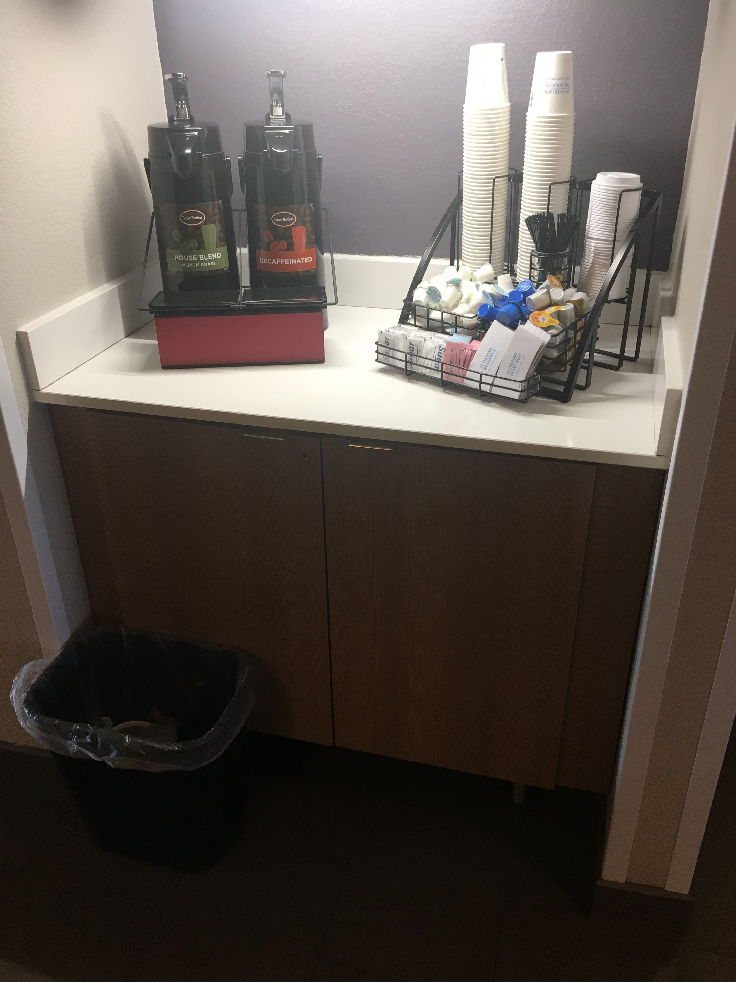 Una kitchenette con cafetera, dispensador de café y una pila de vasos desechables.