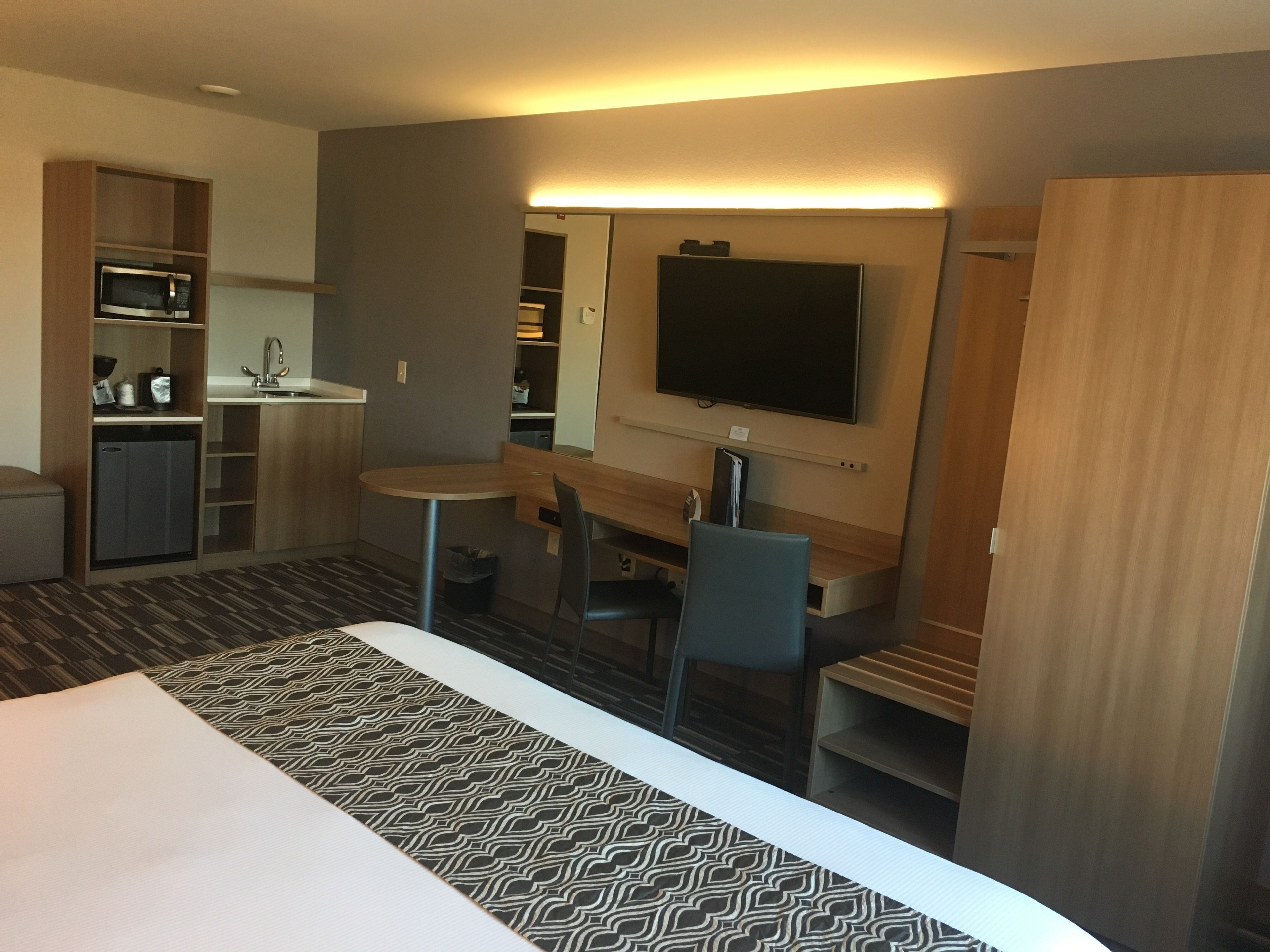 Habitación de hotel con cama, escritorio, silla, televisión, pequeña cocina y baño.