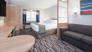 A hotel room with a bed, a sofa, a desk, and a TV. - Microtel Inn & Suites By Wyndham Moorhead Fargo Area (Moorhead)