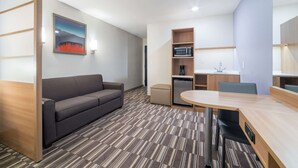 A modern hotel room with a sofa, a dining table, a microwave, and a small kitchenette. - Microtel Inn & Suites By Wyndham Moorhead Fargo Area (Moorhead)