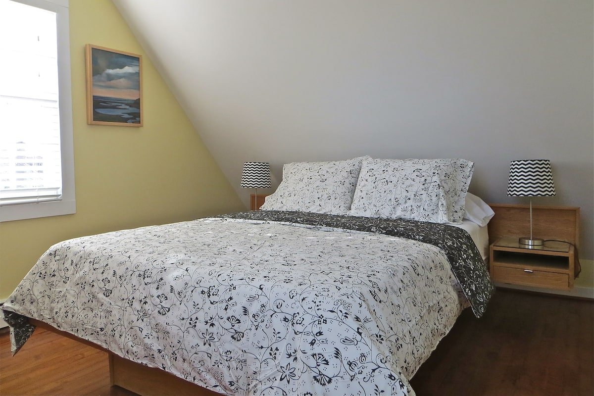 A bedroom with a bed, two bedside lamps, a nightstand, and a window with blinds.