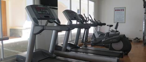 Un gimnasio con cintas de correr, elípticas y una bicicleta estática.