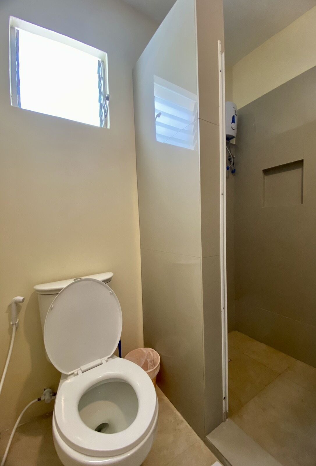 A bathroom with a toilet, a shower, and a window.