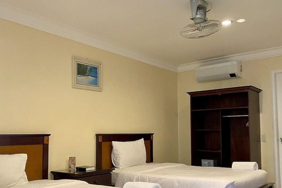 Une chambre d’hôtel avec deux lits, une armoire, un climatiseur et un ventilateur de plafond.