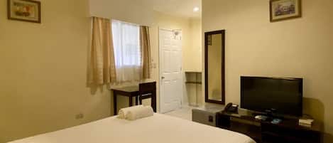 A hotel room with a bed, a desk, a television, a mirror, and a ceiling fan.