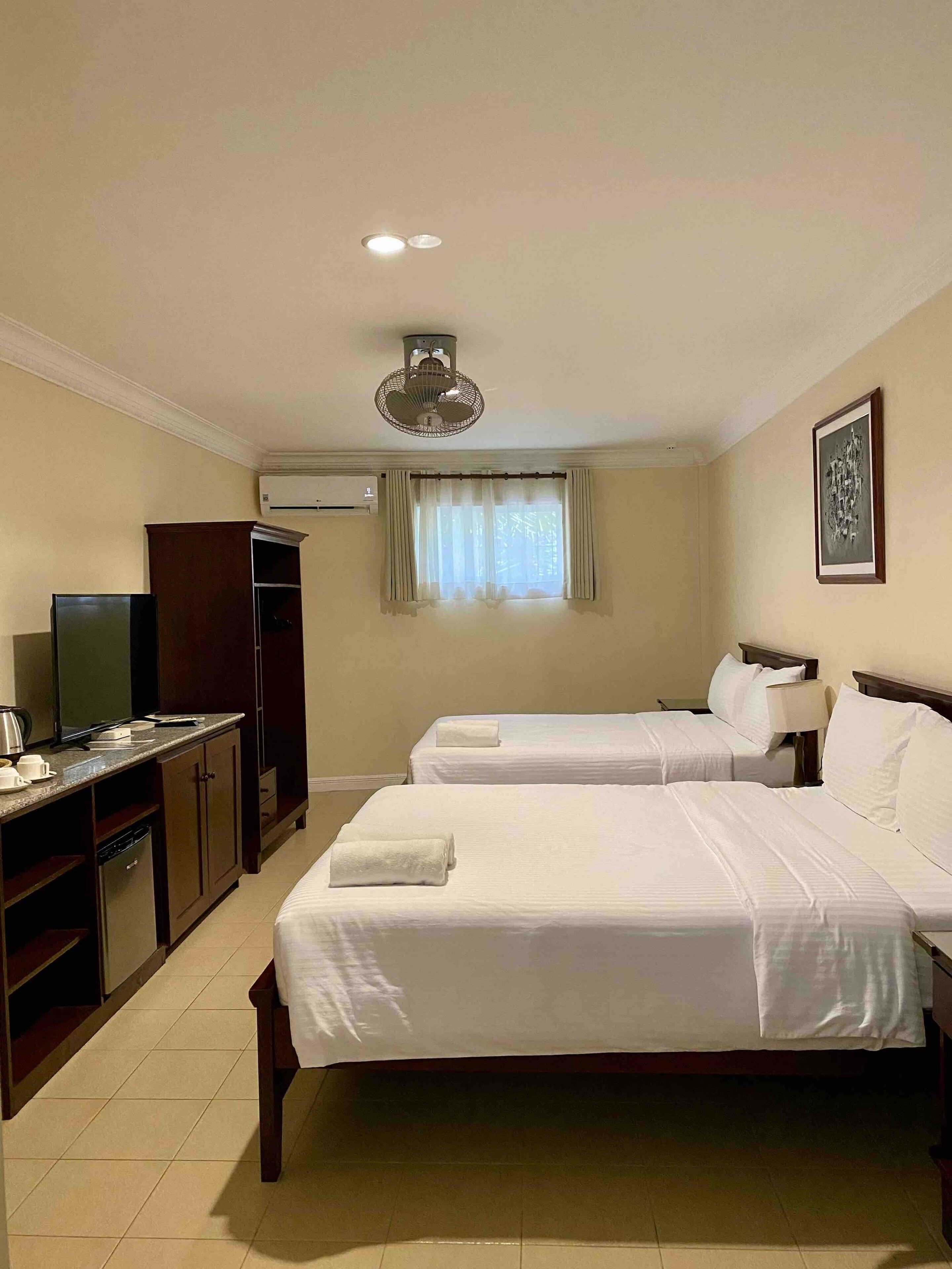 Habitación de hotel con dos camas, un escritorio con televisor, un armario y un equipo de aire acondicionado.