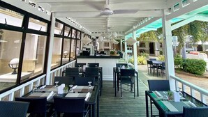 Een overdekt terras met eettafels, stoelen, een bar en grote ramen.