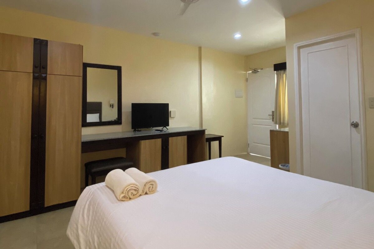 Ein Hotelzimmer mit Bett, Schreibtisch, Spiegel, Deckenventilator und Tür.