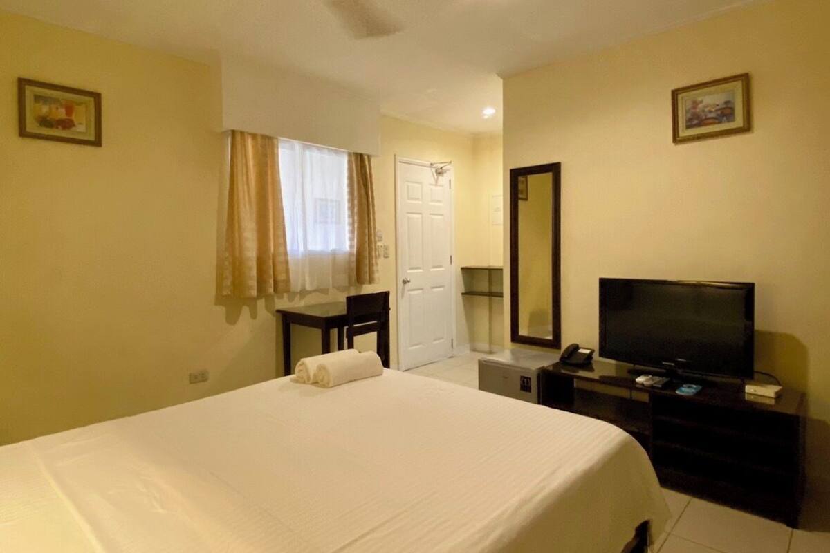 Een hotelkamer met een groot bed, een bureau, een televisie en een plafondventilator.