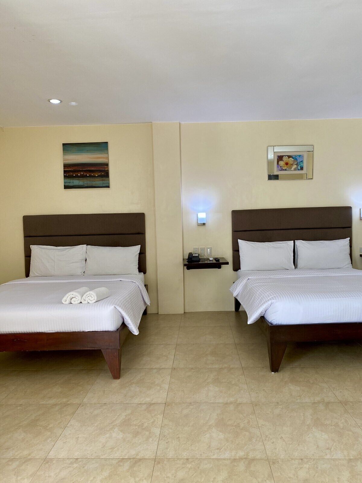 A hotel room with two beds, a painting on the wall, and a small table with a phone.