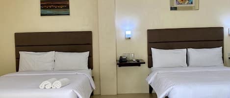 A hotel room with two beds, a painting on the wall, and a small table with a phone.