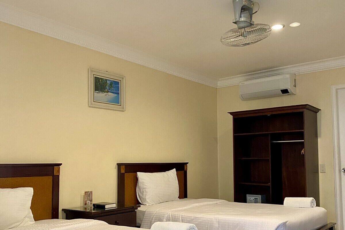 A hotel room with two beds, a wardrobe, an air conditioning unit, and a ceiling fan.