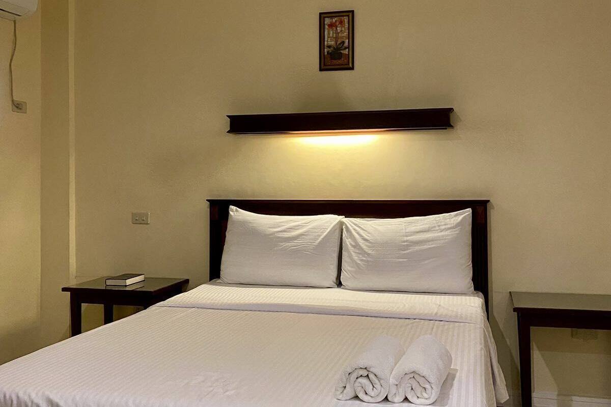 A neatly made bed with white linens, a ceiling fan, and a bedside table with a book.