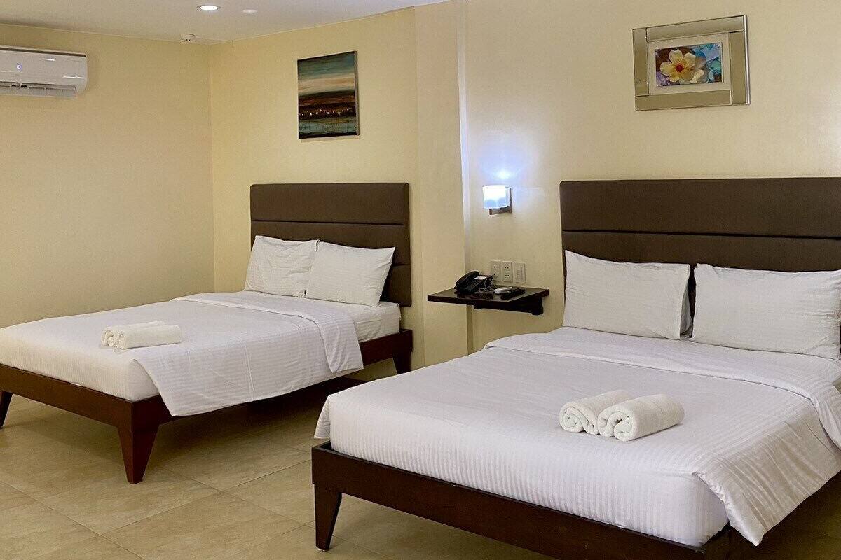 A hotel room with two beds, a nightstand, an air conditioning unit, and a painting on the wall.