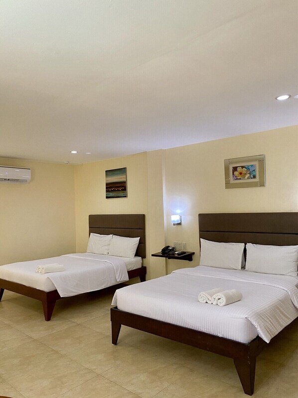 Habitación de hotel con dos camas, una mesita de noche, un equipo de aire acondicionado y un cuadro colgado en la pared.