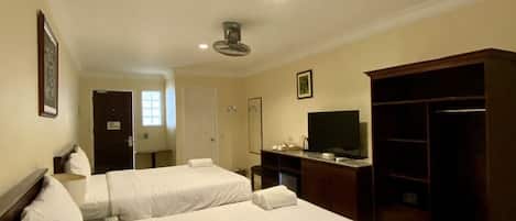 Ein Hotelzimmer mit zwei Betten, einem Fernseher, einem Kleiderschrank und einem Deckenventilator.