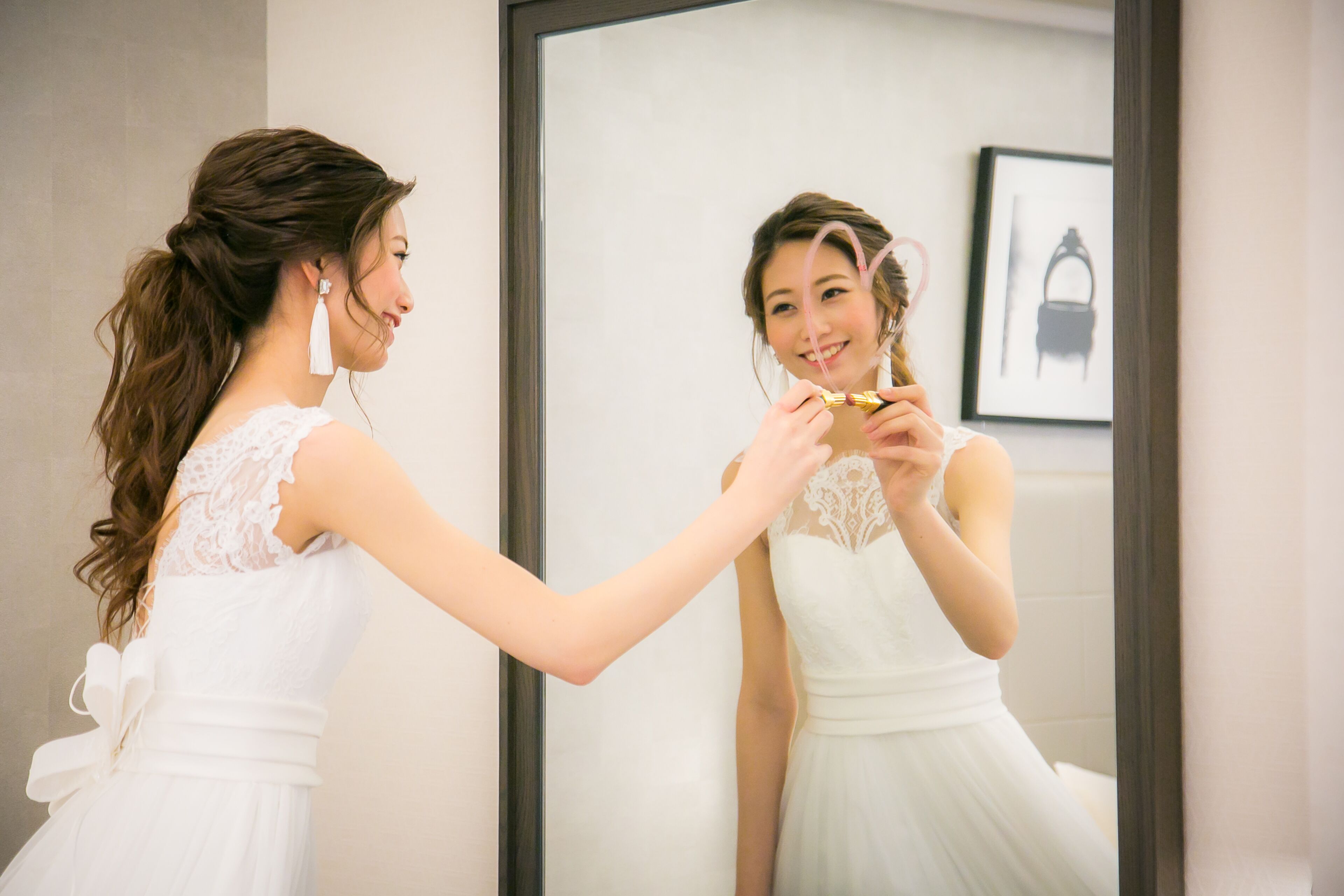 Una persona con vestido blanco arreglándose el cabello frente a un espejo.