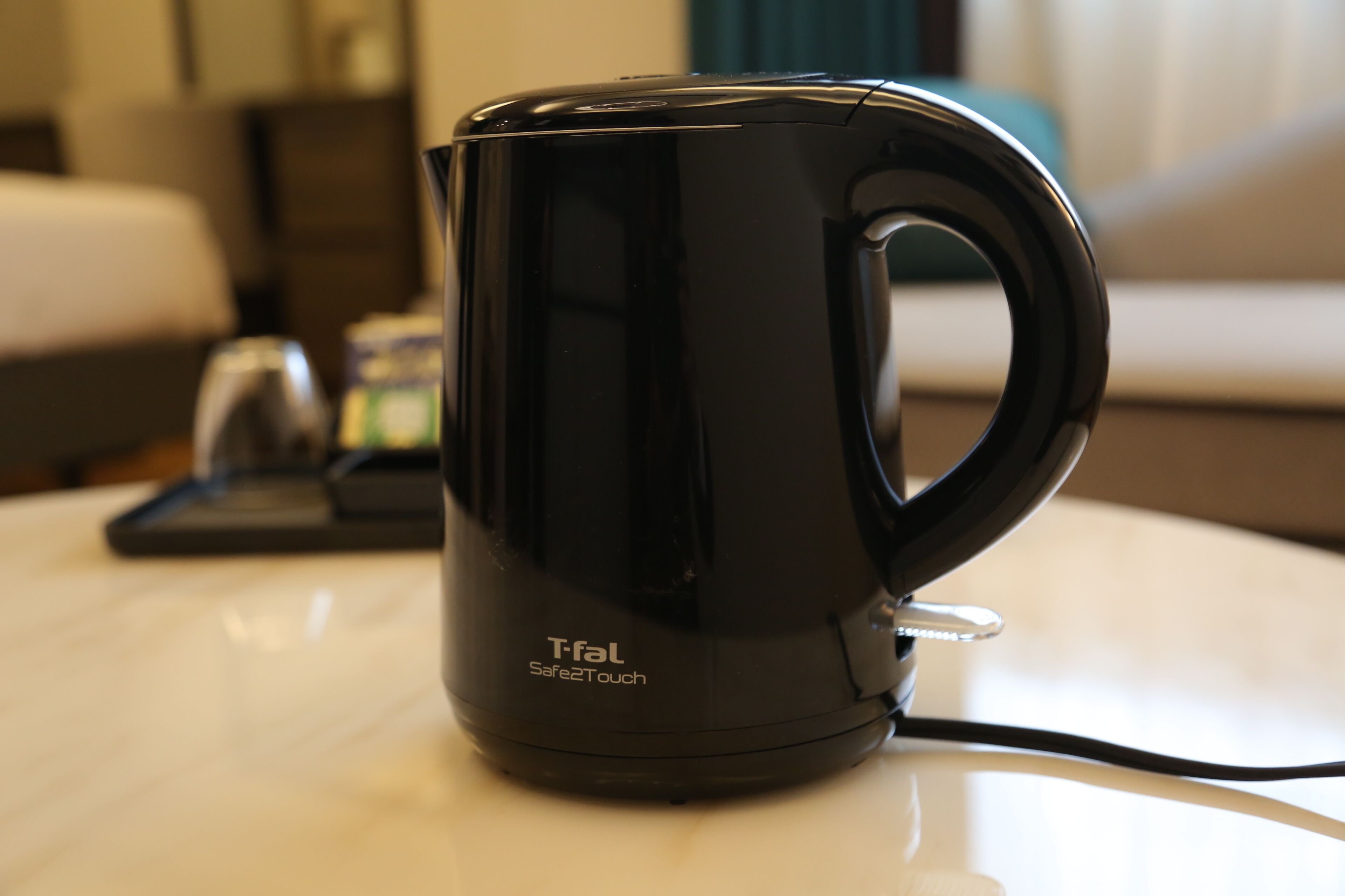 A black electric kettle on a white table with a cord.