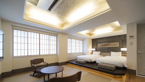 Habitación de hotel con cama, dos sillas, una mesita y ventanas amplias.