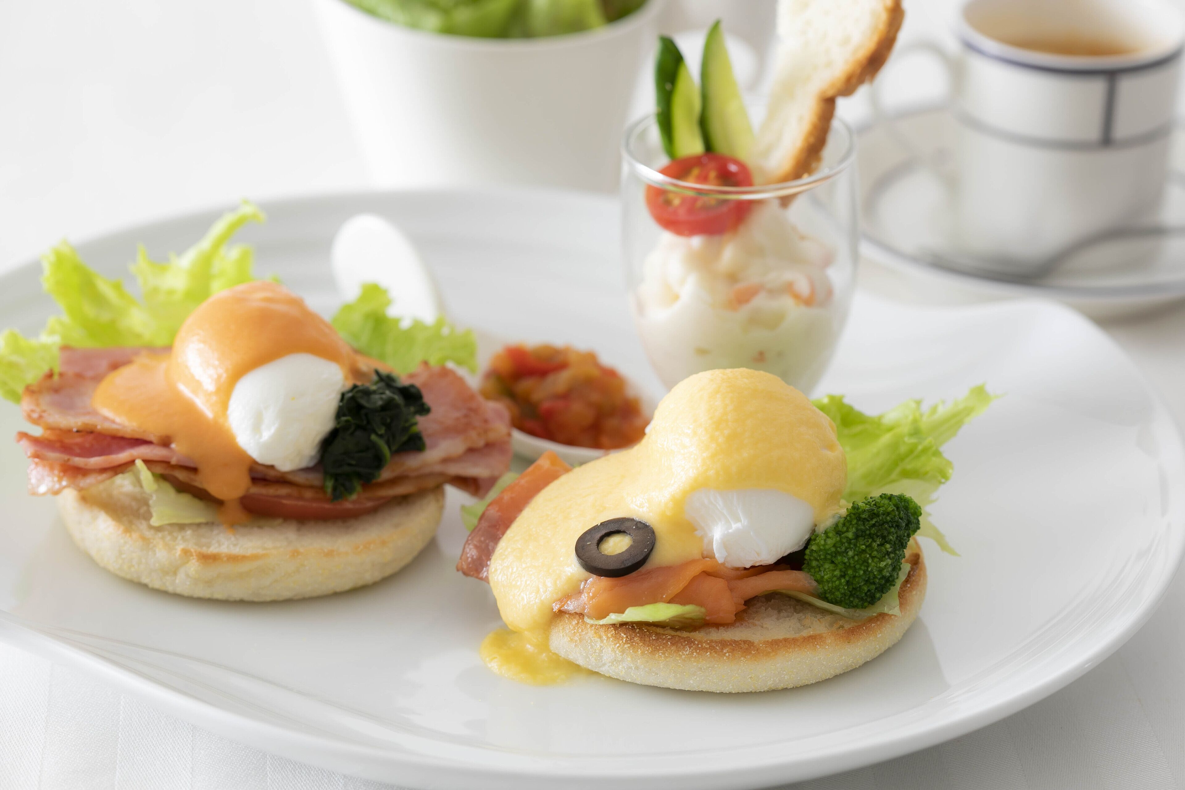 Two eggs benedict sandwiches on a white plate with a side of salad and a cup of coffee.