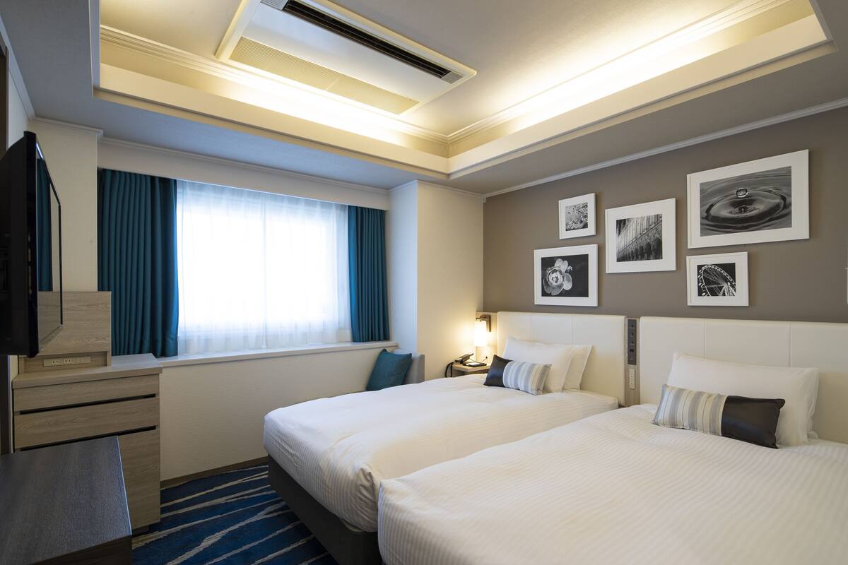 Habitación de hotel con dos camas, un escritorio, un televisor y una ventana con cortinas.