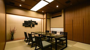 Una sala de reuniones tradicional japonesa con suelo de tatami, una mesa baja y sillas de madera oscura.