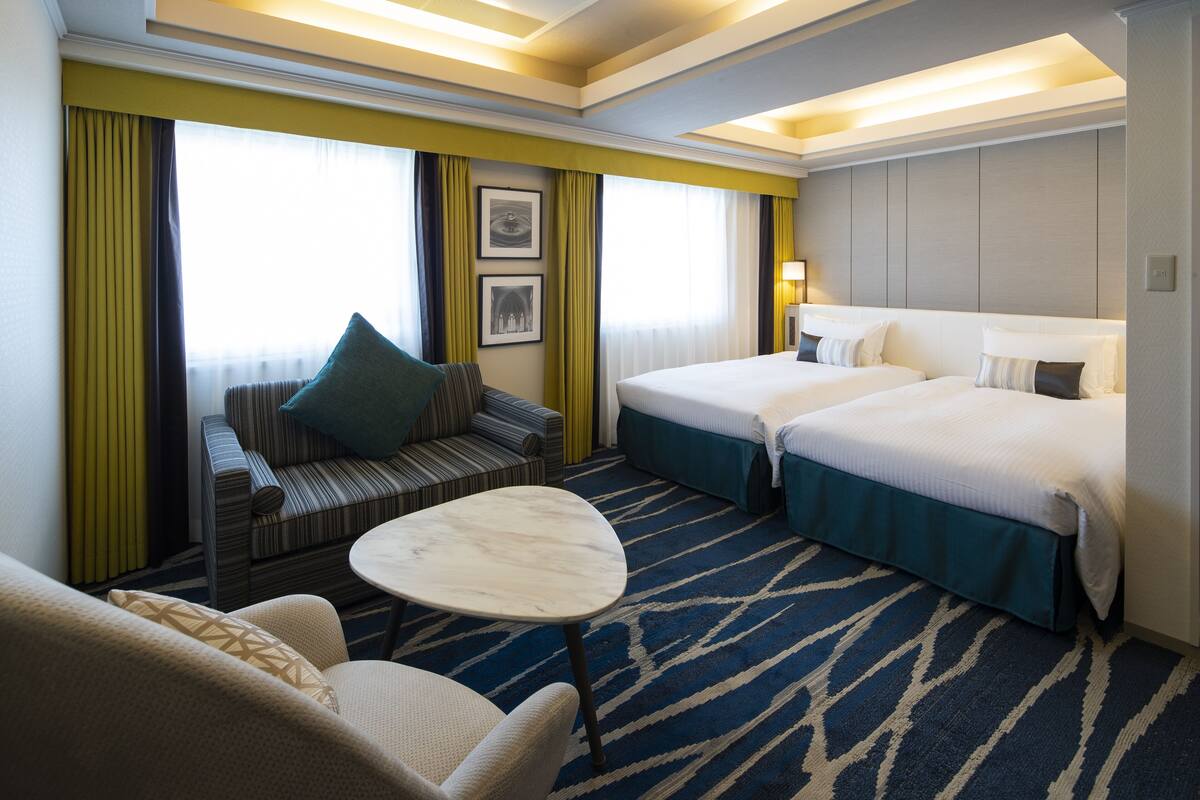 Habitación de hotel con sofá, dos camas individuales, una mesita y vistas a la ciudad.