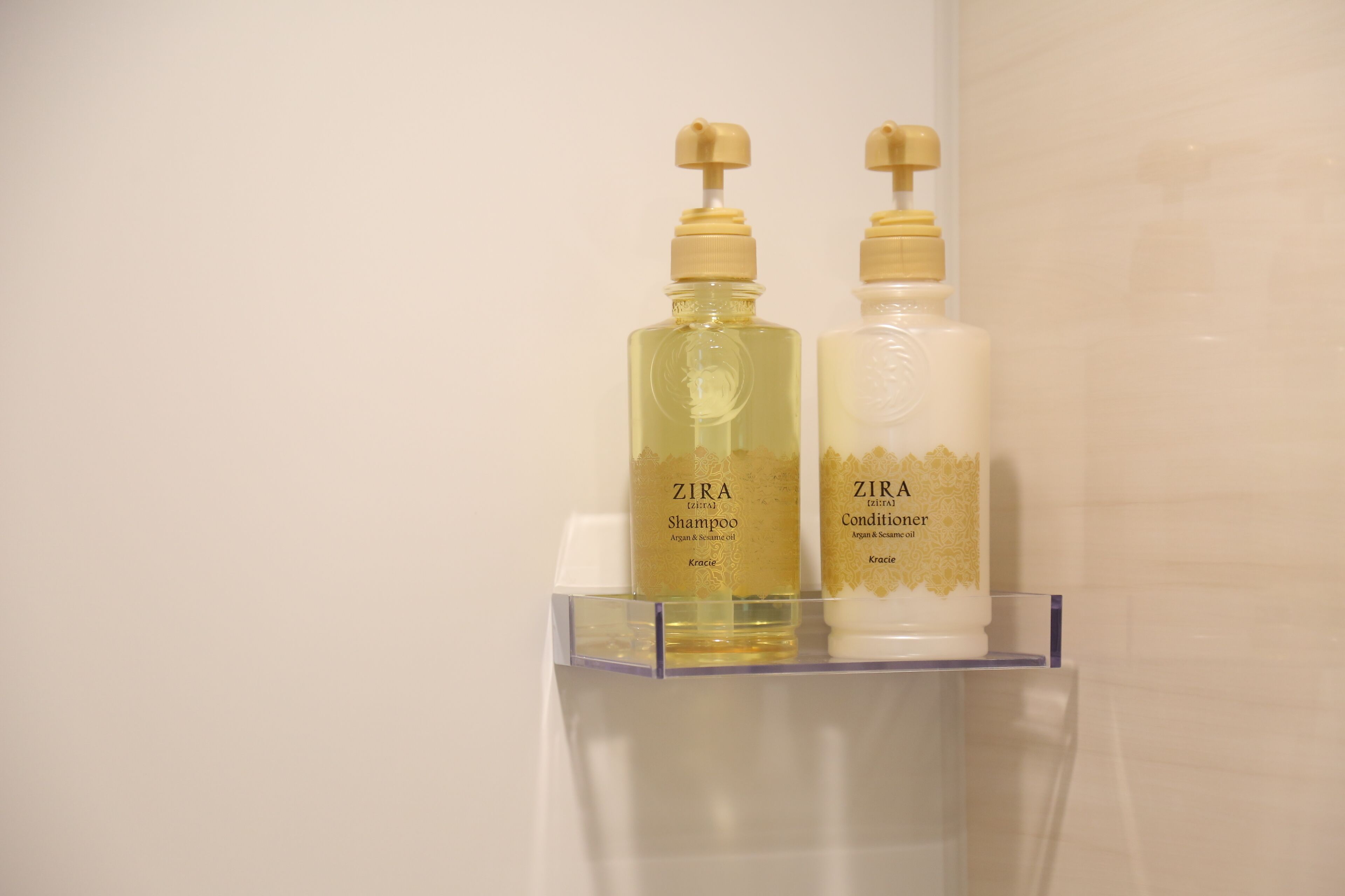 Dos botellas de champú y acondicionador ZIRA sobre una estantería transparente.