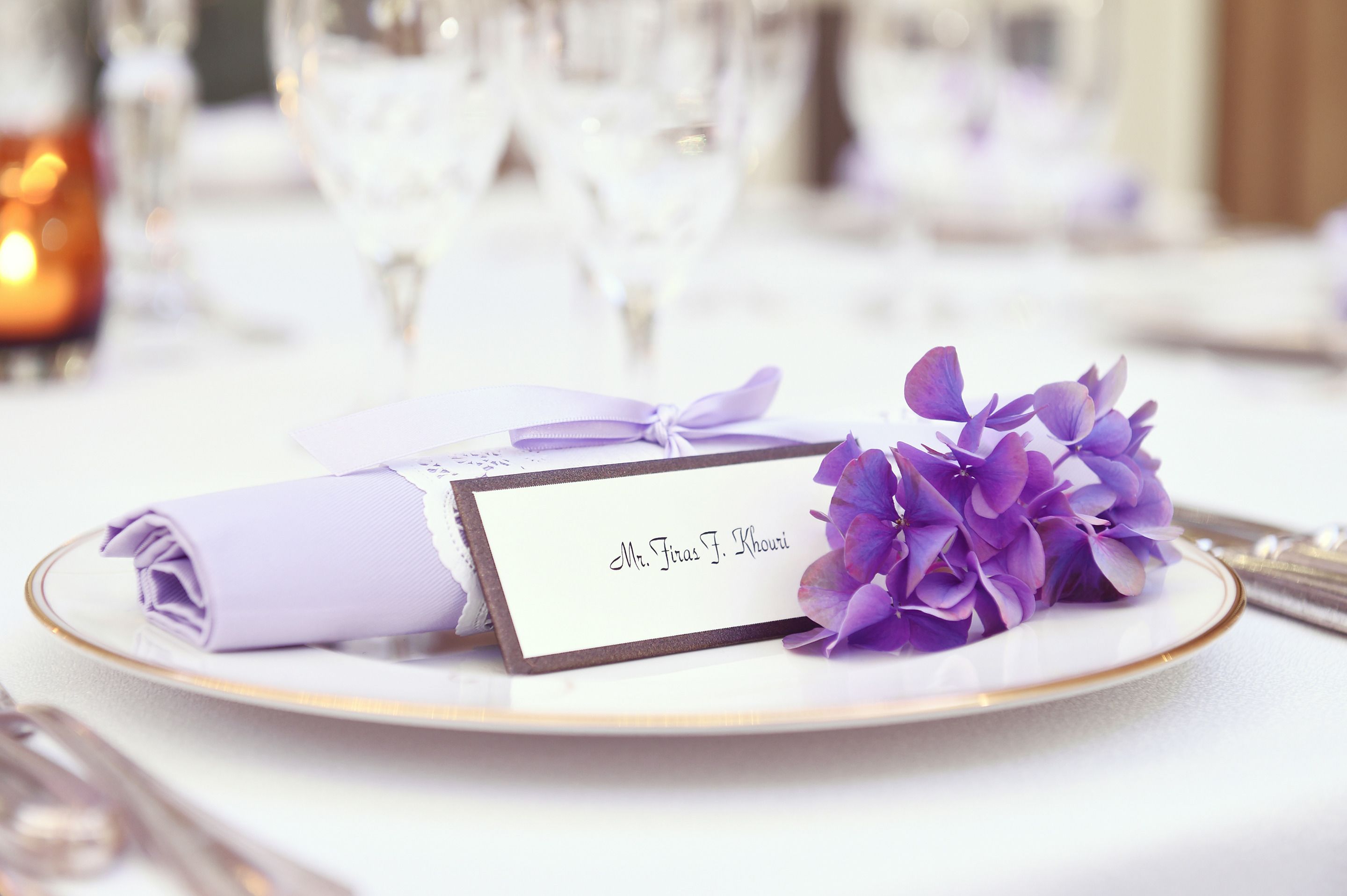 A table setting with a name card, a folded napkin, and a purple flower arrangement.