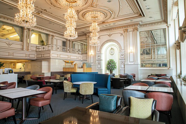 Un restaurante espacioso con techos altos, candelabros ornamentales y una variedad de opciones de asientos, incluyendo cabinas y mesas.