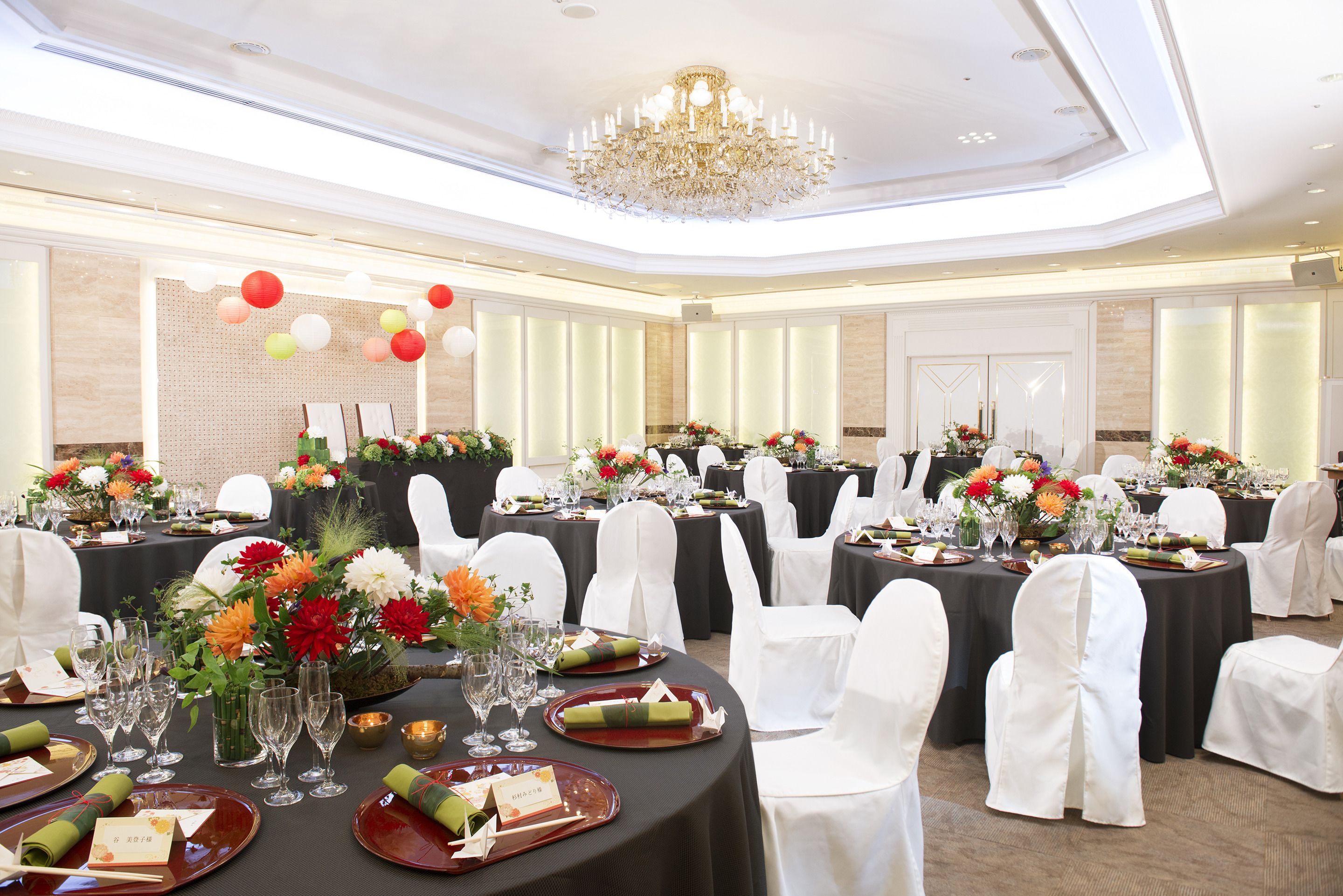 A banquet hall with round tables, white chairs, and floral centerpieces.